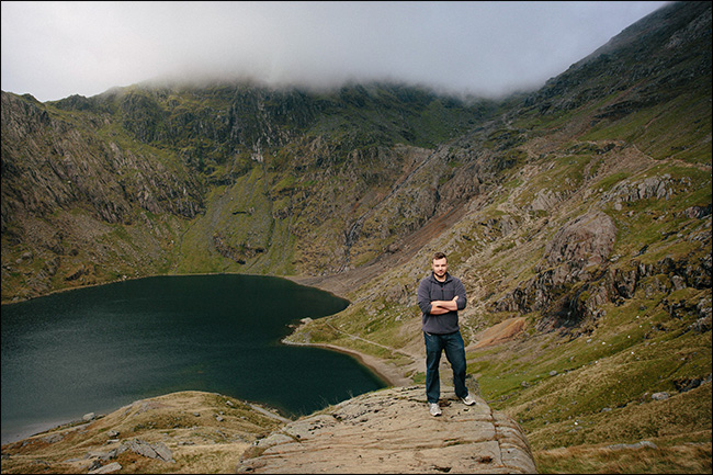 Un amplio retrato de un hombre de pie en un cañón cerca de un lago.