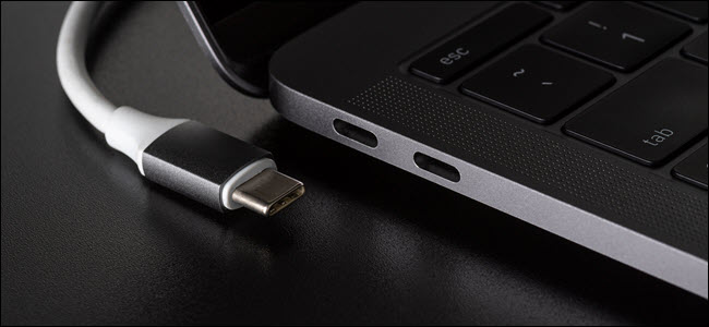 Cable USB-C junto a un portátil plateado sobre un escritorio negro brillante.