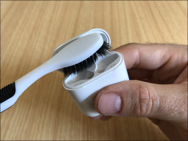 La mano de un hombre sostiene un estuche de carga de AirPods y lo limpia con un cepillo de dientes.