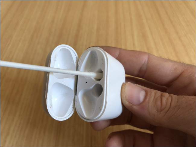 La mano de un hombre sosteniendo un estuche de carga AirPods y limpiando los canales de carga con un hisopo.