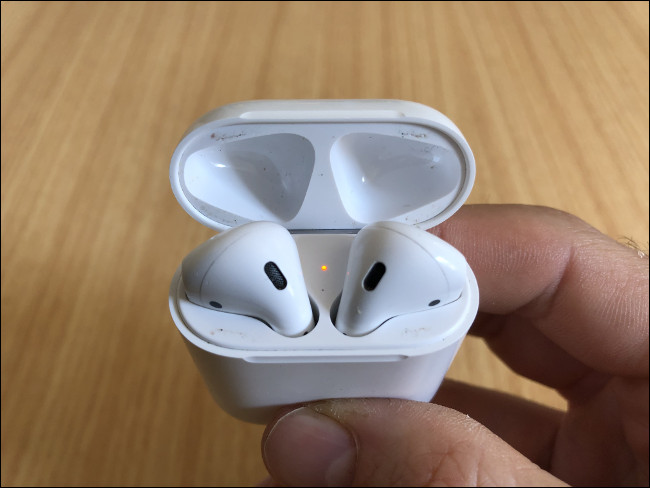 La mano de un hombre sosteniendo un par de AirPods descansando en su estuche de carga.