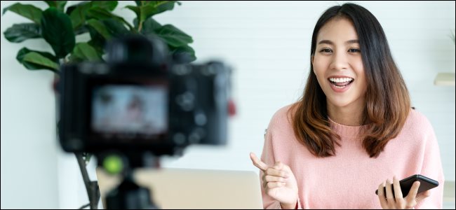 Una mujer filmando un video con una cámara frente a una computadora portátil.