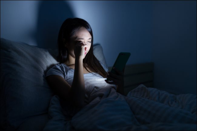 Una mujer que usa un teléfono inteligente en la cama por la noche.