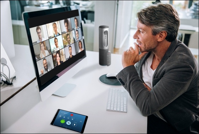 Un hombre en una reunión de Zoom en su Mac con los participantes en la vista de galería en el monitor. 