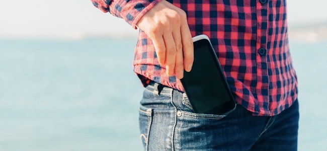 La mujer saca el teléfono móvil de su bolsillo de jeans en la playa cerca del mar para hacer un autorretrato o fotografiar el mar