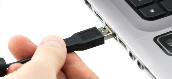 Una mano conectando un cable USB tipo A a una computadora portátil.