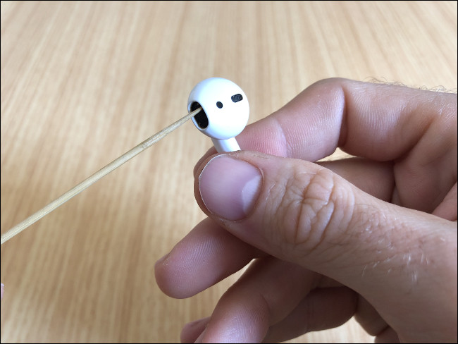 La mano de un hombre sosteniendo un AirPod y limpiando el altavoz con Toothpick.