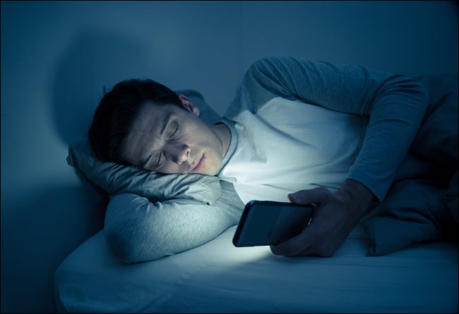 Un hombre enviando mensajes de texto en su teléfono inteligente en la cama por la noche.