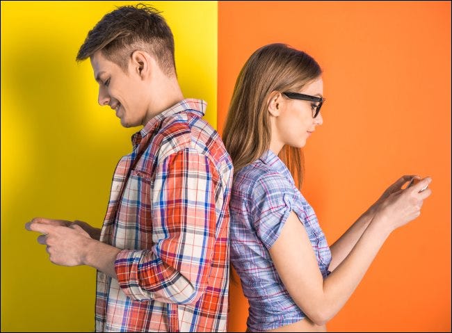 Una pareja de pie espalda con espalda mientras envía mensajes de texto.
