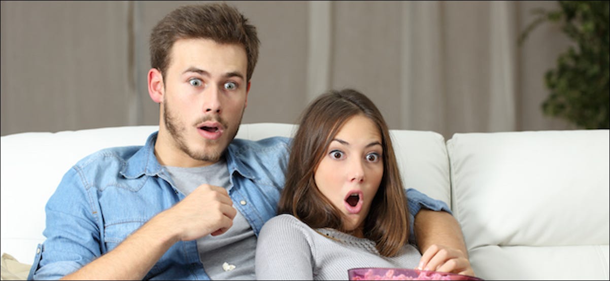 Pareja asombrada viendo un reality show de televisión sentado en un sofá en casa