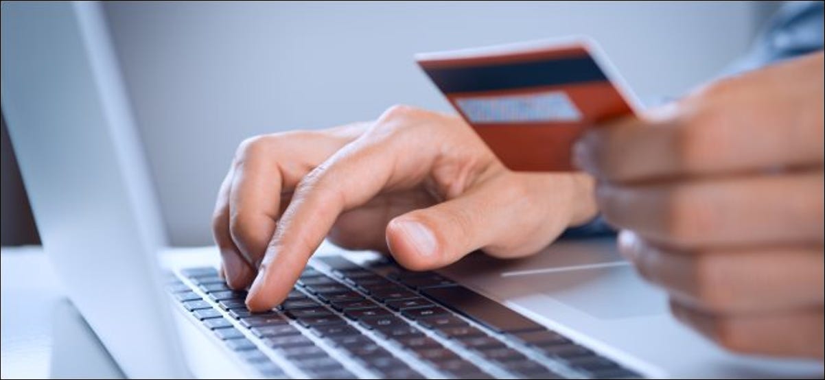 Una persona que tiene una tarjeta de crédito o débito mientras escribe en una computadora portátil.