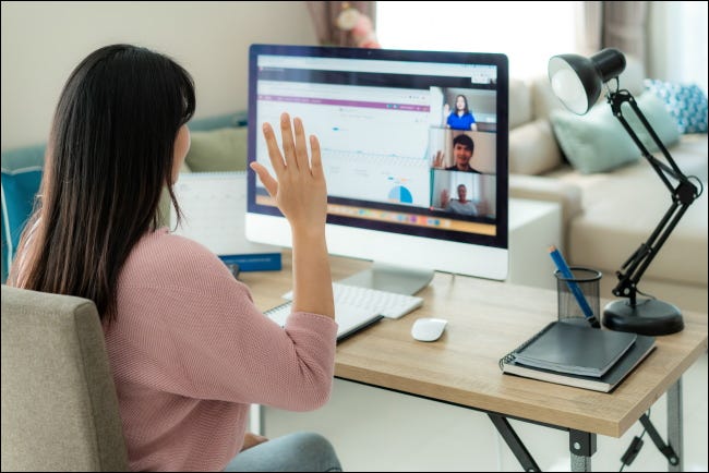Una mujer saludando a una computadora durante una videollamada.