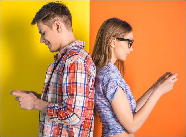 Una joven pareja de pie espalda con espalda mientras usa sus teléfonos.