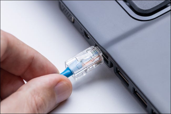 Una mano conectando un cable Ethernet a una computadora portátil.