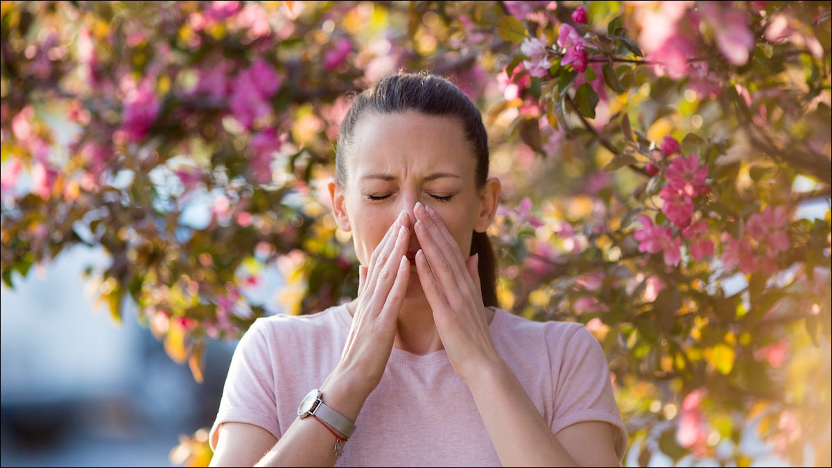 Mujer de pie bajo un árbol estornudando por alergias al polen