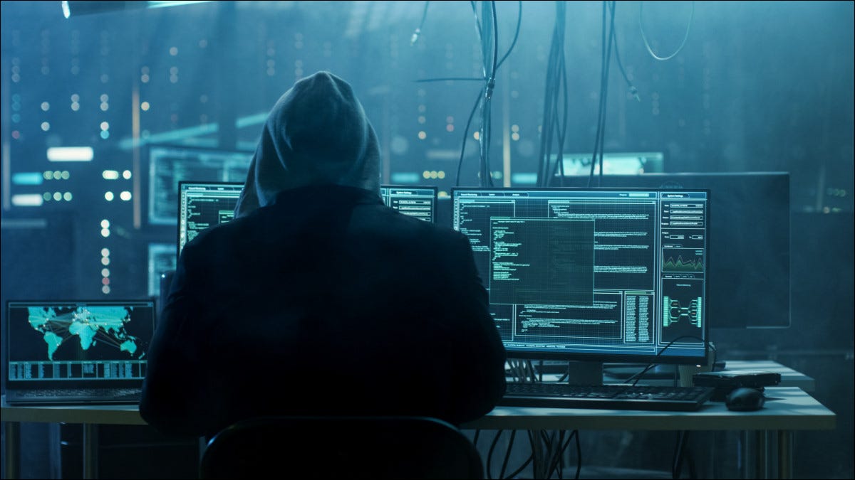 Un hacker encapuchado sentado frente a las computadoras.