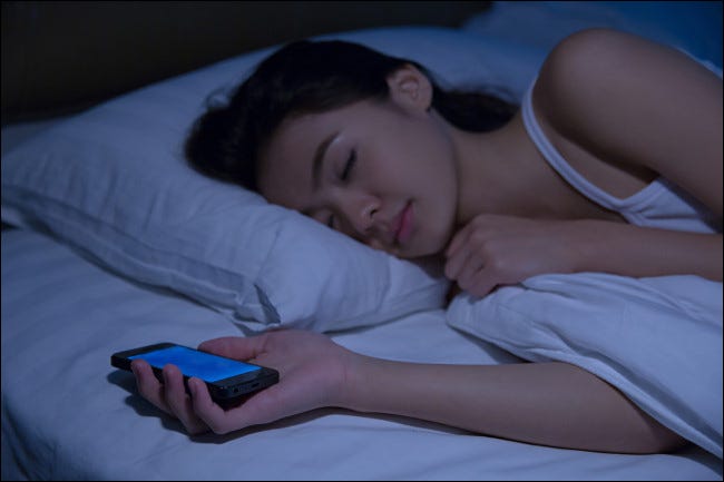 Una mujer durmiendo mientras sostiene un teléfono inteligente.