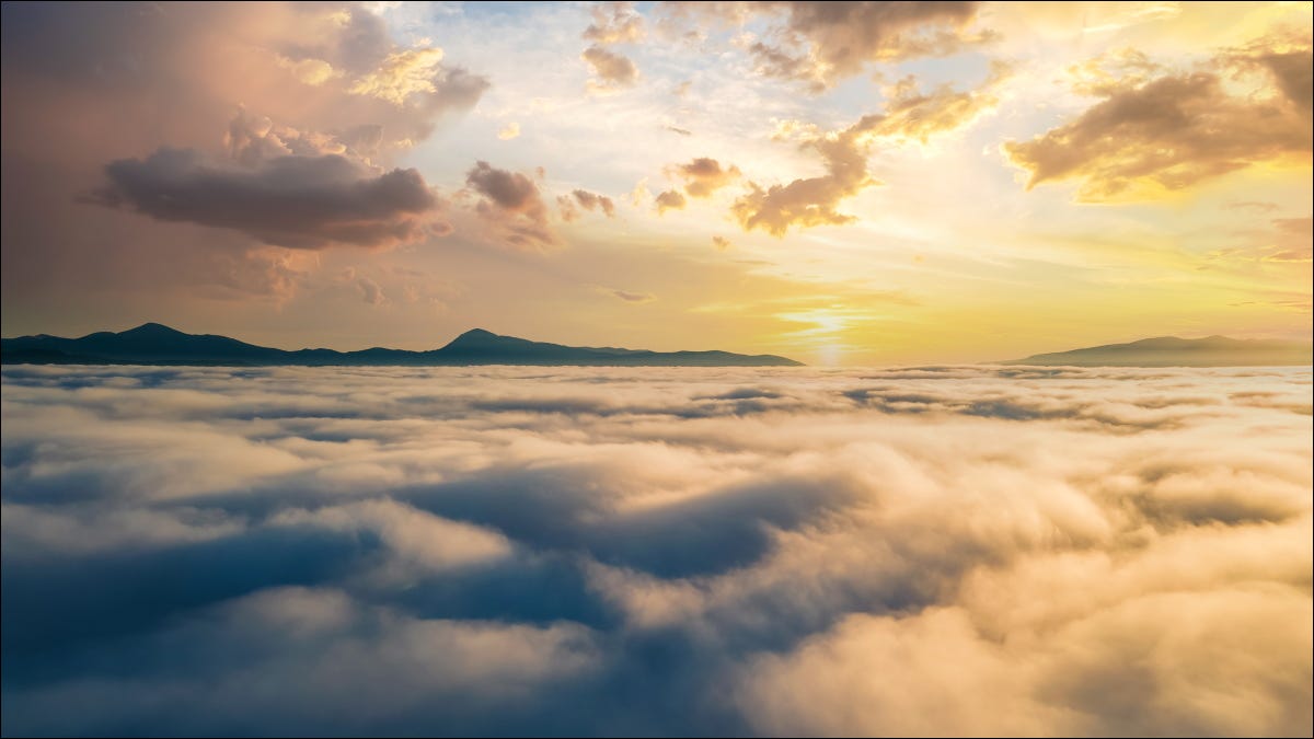 Una vista aérea de una puesta de sol sobre densas nubes con montañas en el horizonte.