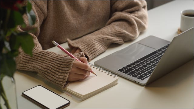 Mujer tomando notas en papel junto a una computadora portátil