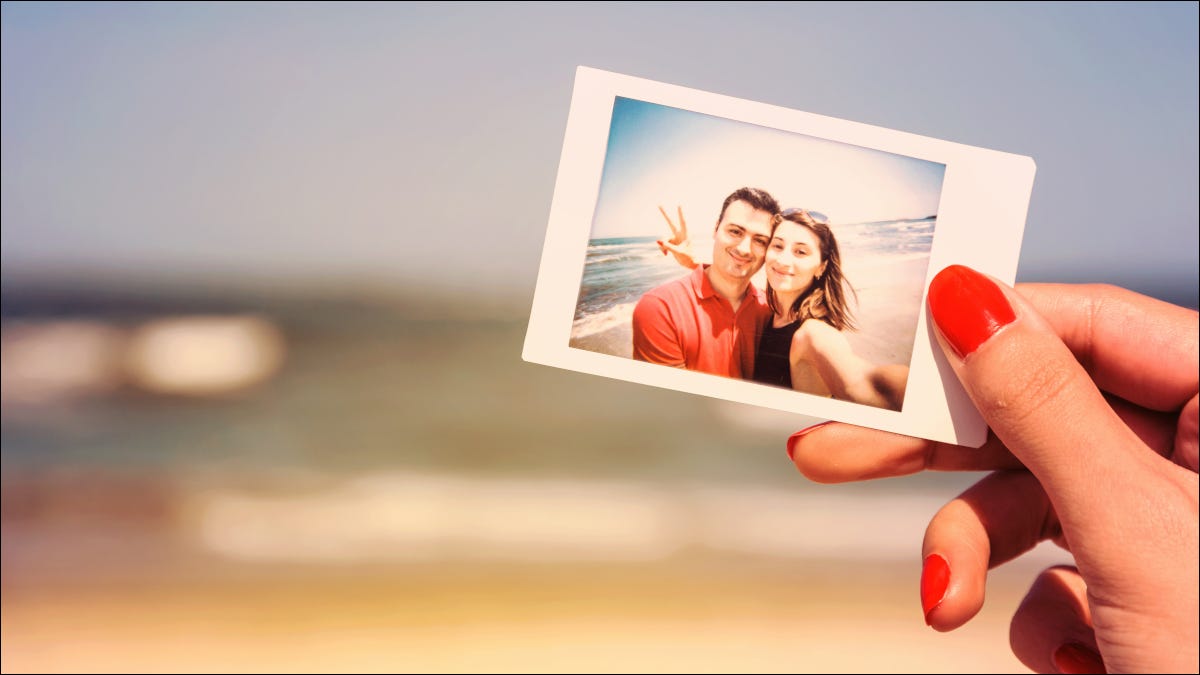 Mano de mujer sosteniendo la fotografía de la pareja en frente de la playa