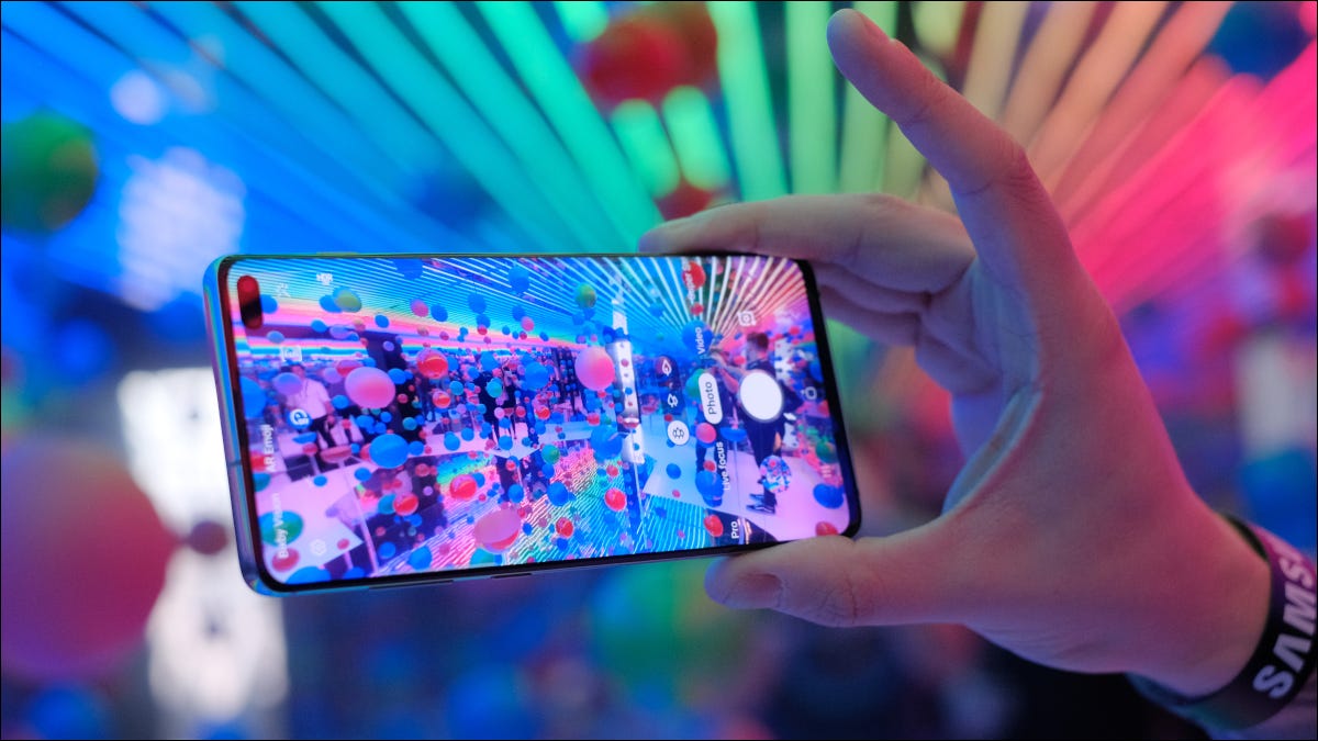 Mano sosteniendo un Samsung Galaxy S10 con una pantalla colorida frente a luces multicolores.