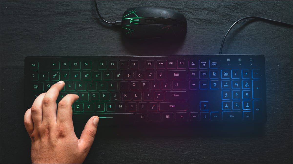 Teclado y ratón de color RGB con la mano en el teclado