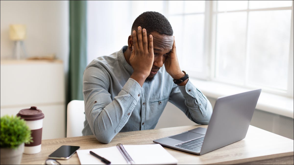 Hombre sentado en el escritorio con un portátil, agarrándose la cabeza con frustración
