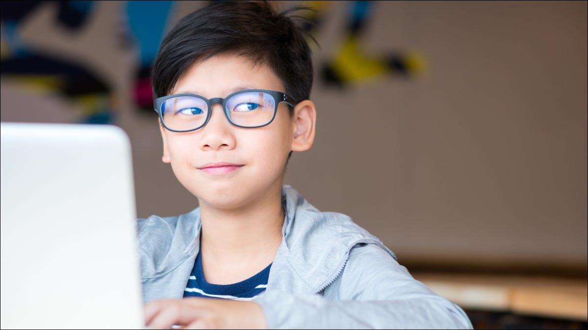 Niño preadolescente con gafas en un portátil sonriendo y poniendo los ojos en blanco
