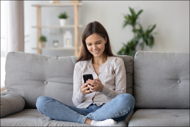 Adolescente sonriendo y sentado en el sofá con smartphone