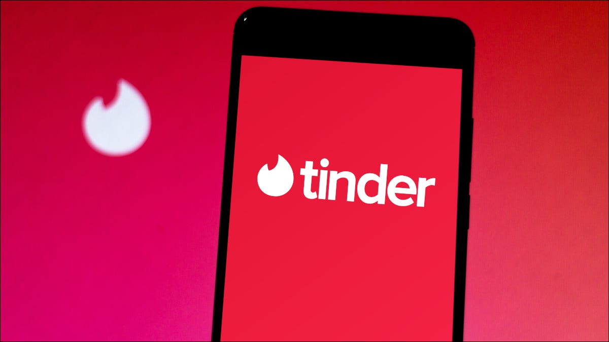 Smartphone que muestra el logotipo de la aplicación Tinder sobre un fondo rojo.
