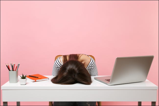 Mujer agotada con rostro plantado en el escritorio junto a la computadora y suministros de oficina.