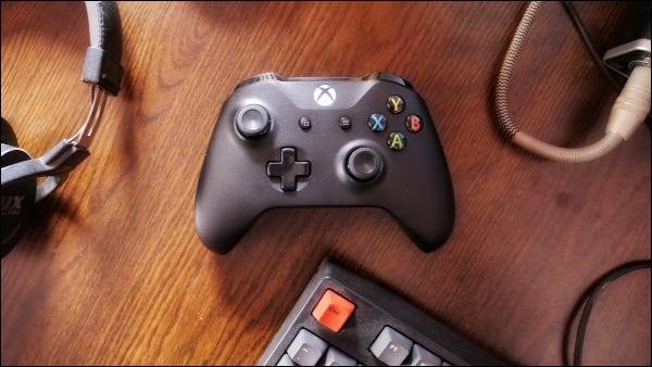 Controlador Xbox One con auriculares y teclado en superficie de madera.