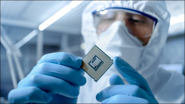 Hombre en traje estéril examinando un microchip en una fábrica.