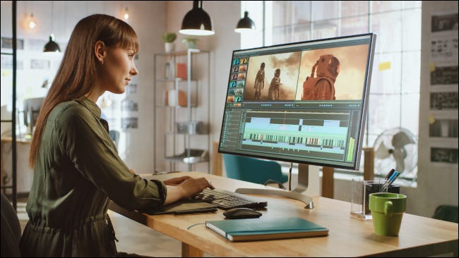 Mujer editando videos en un monitor de computadora grande