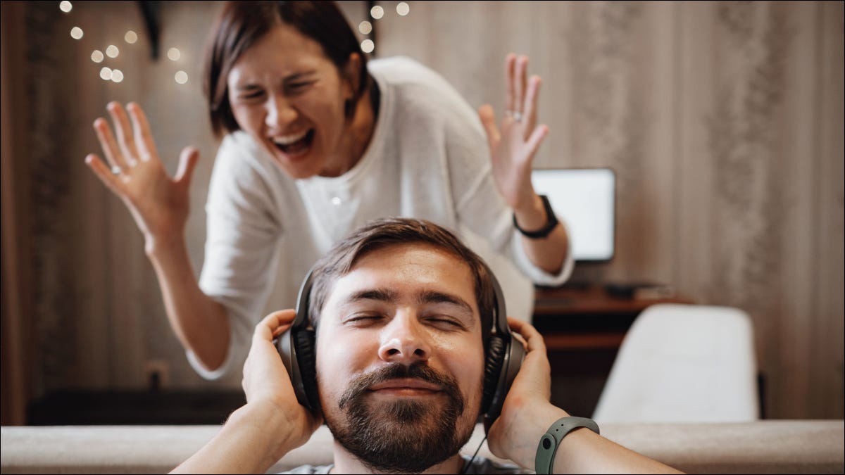 Hombre con auriculares con una sonrisa mientras una mujer grita de rabia.