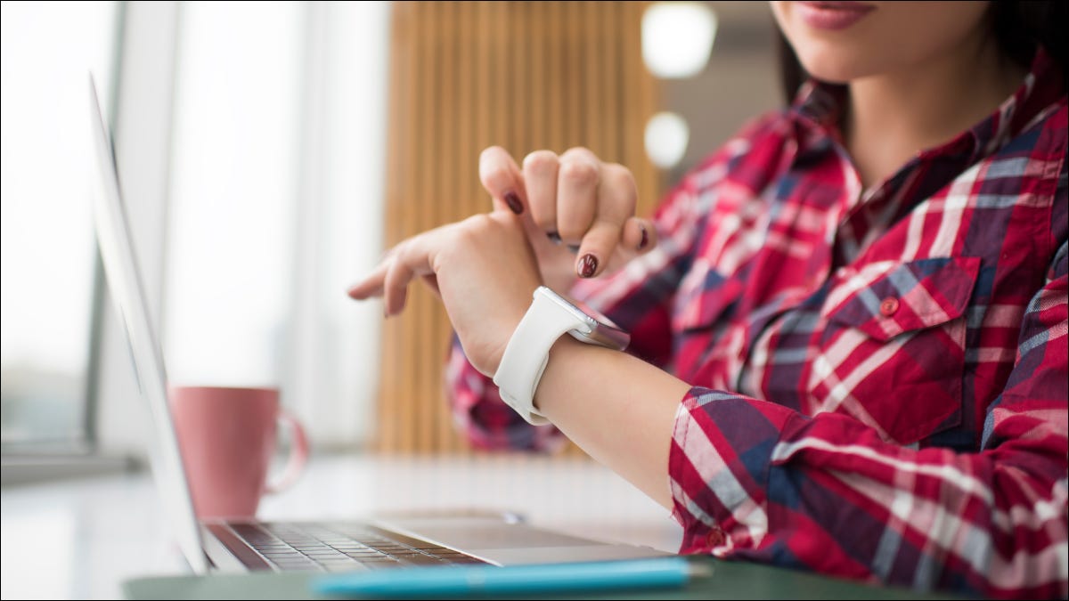 Mujer mirando smartwatch mientras usa una computadora portátil