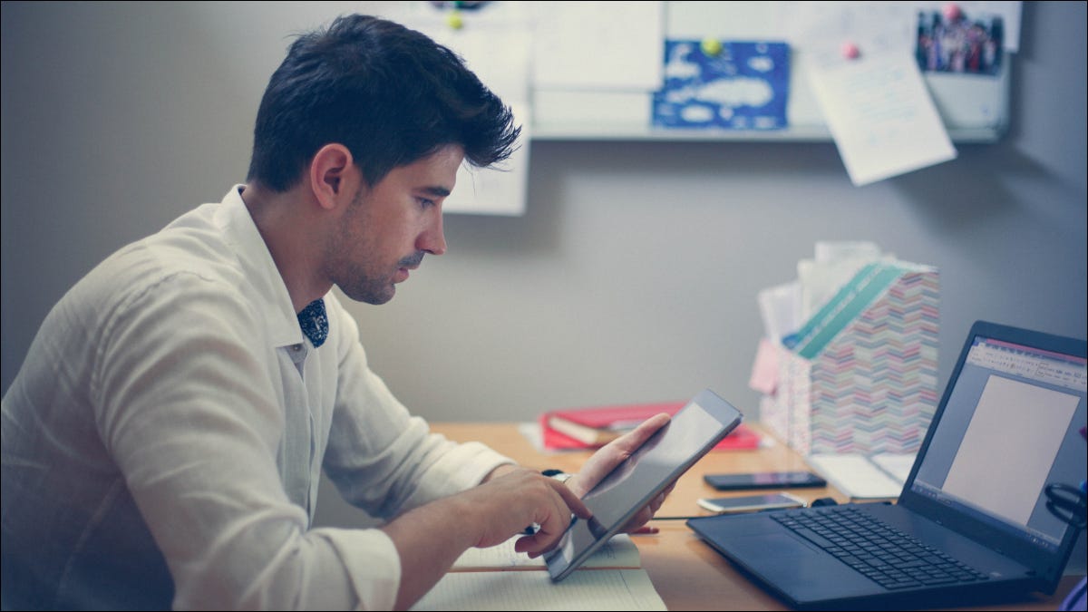 Hombre que usa una tableta con una computadora portátil frente a él.