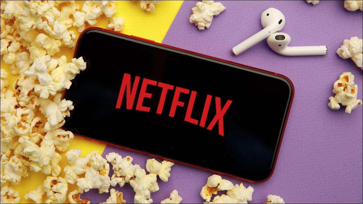 Logotipo de Netflix en un iPhone y junto a AirPods y palomitas de maíz