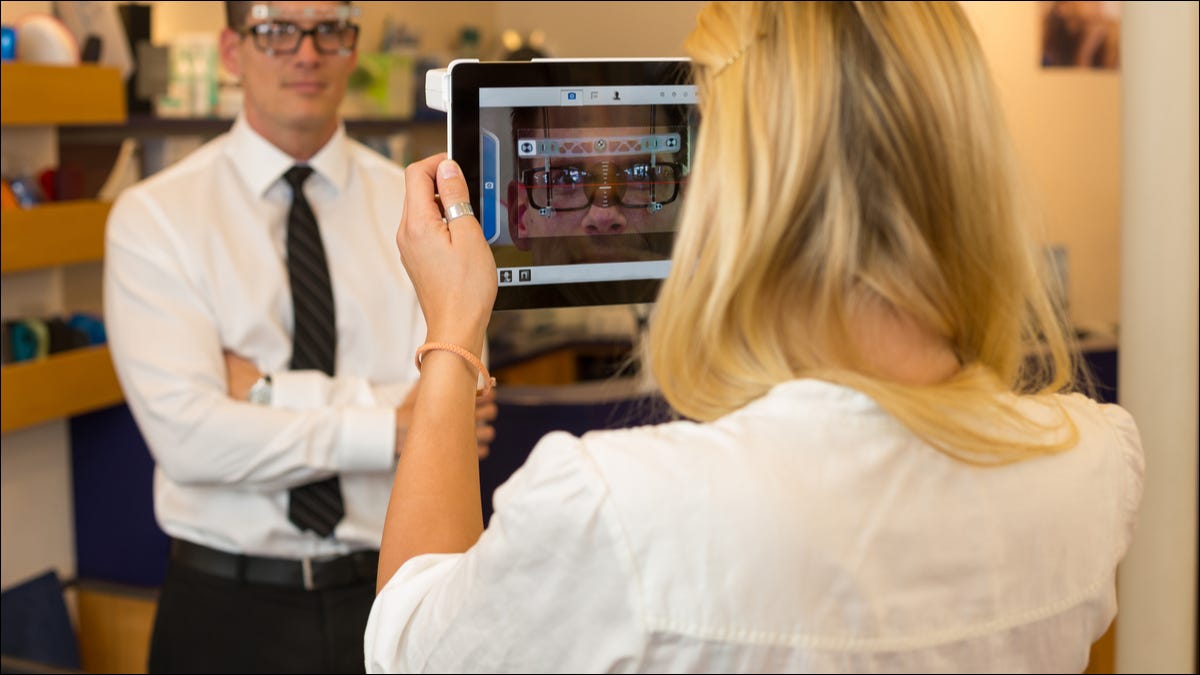 Un optometrista que mide la distancia del ojo de un hombre con una tableta y una cámara.