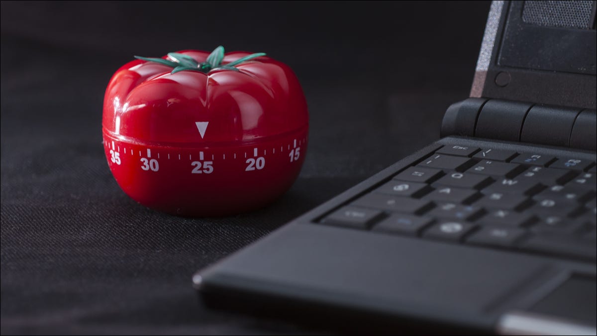Un temporizador mecánico en forma de tomate junto a una computadora portátil.