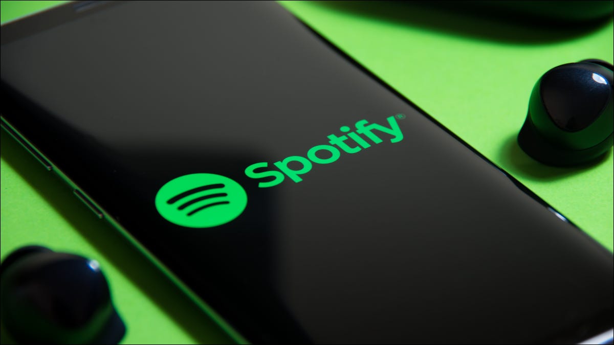 Smartphone que muestra el logotipo de Spotify junto a los auriculares inalámbricos sobre un fondo verde.