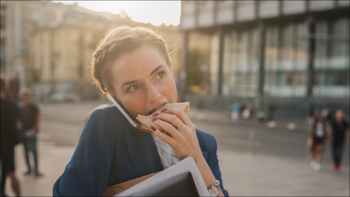 Mujer ocupada comiendo un sándwich y hablando por celular al mismo tiempo.