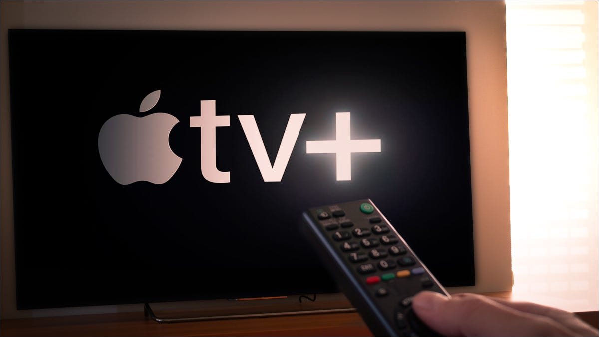 Primer plano de un control remoto de TV frente a un televisor con el logotipo de Apple TV+.