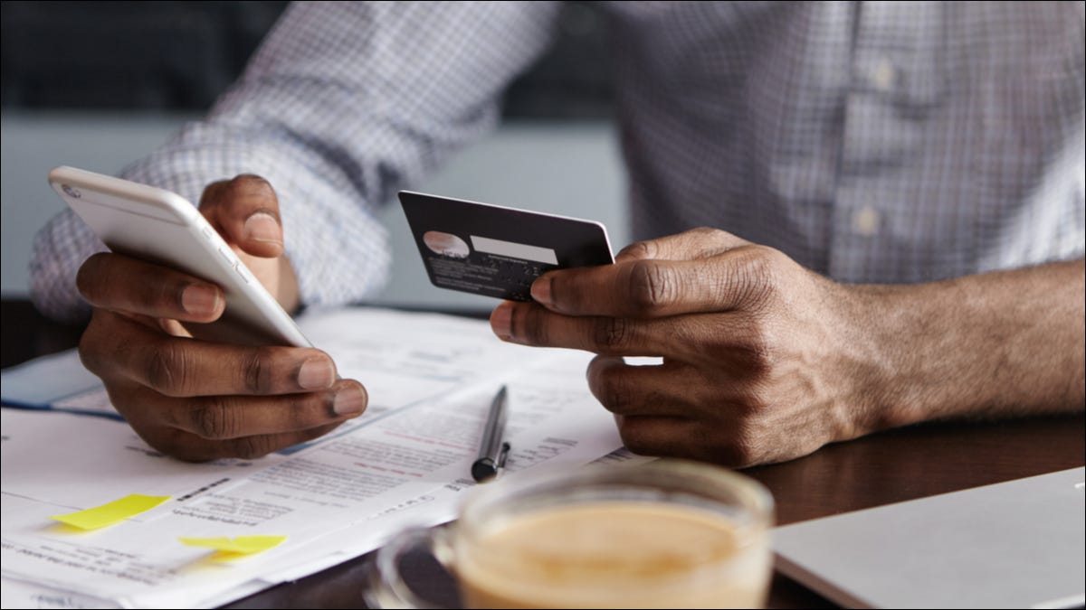 Un hombre que realiza operaciones bancarias en un teléfono con una tarjeta de crédito en la mano