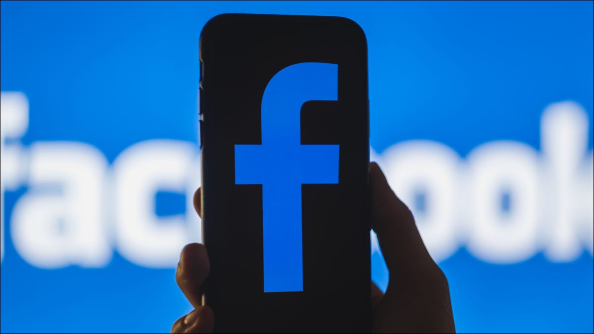 Un teléfono inteligente con una versión oscura del logotipo de Facebook frente a un banner de Facebook
