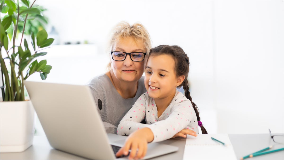 Una mujer ayuda a un niño a usar una computadora portátil.