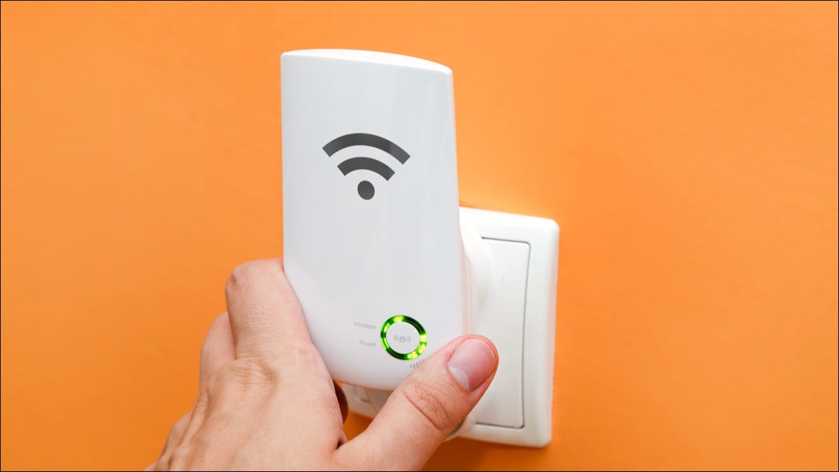 Una mano agarrando un repetidor Wi-Fi en un enchufe eléctrico.