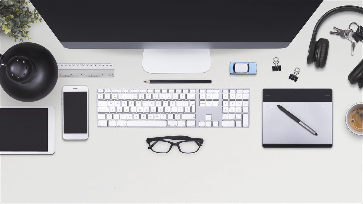 Un escritorio de oficina con una computadora, un teléfono inteligente con teclado, auriculares y más