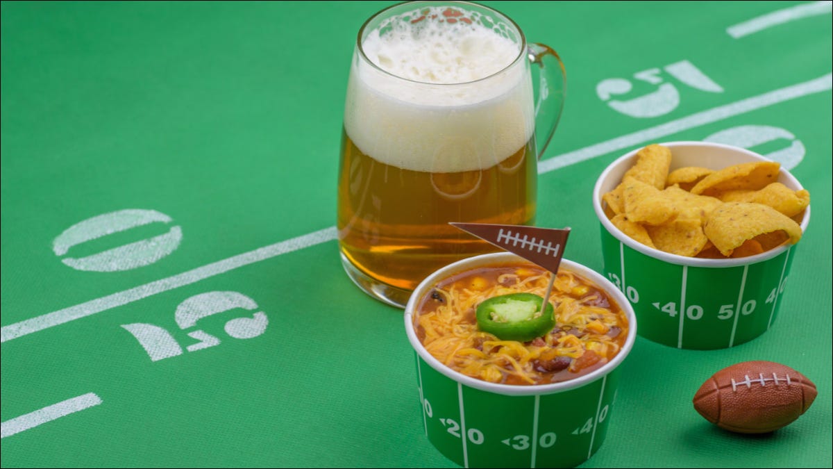 Mesa con temática de fútbol con tazones de chili con temática de fútbol y un vaso de cerveza