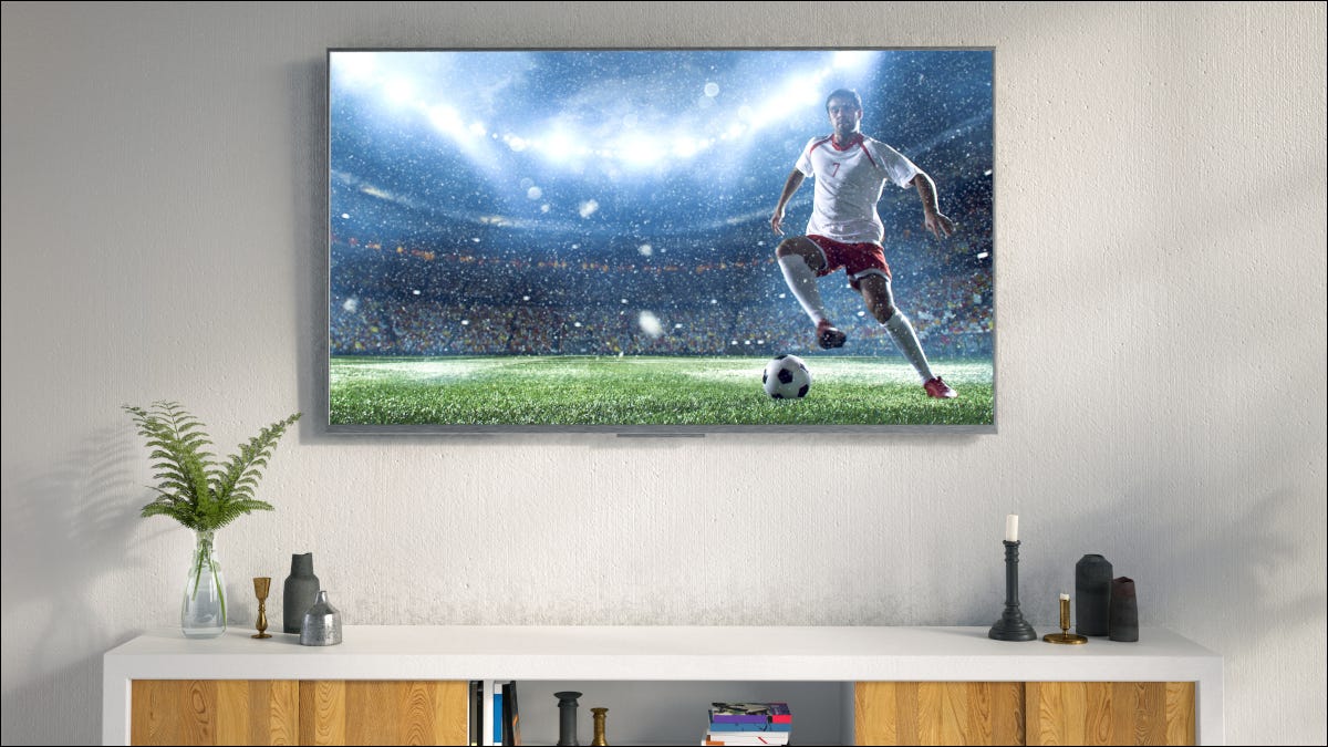 Un televisor LED colgado en la pared de una sala de estar, con un jugador de fútbol en pantalla.